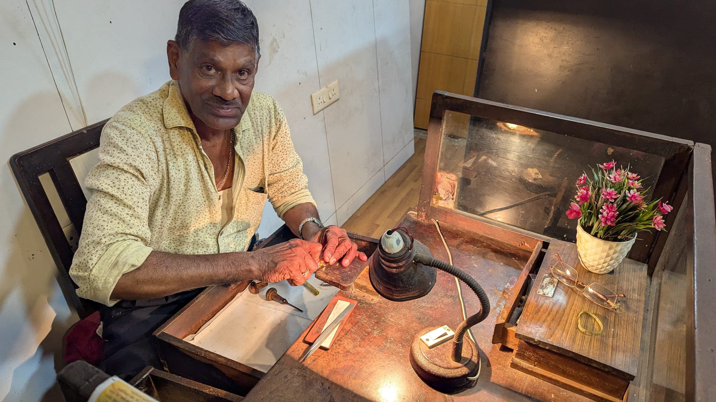 A goldsmith at his wooden workbench under a bench lamp, working on a piece of gold jewellery