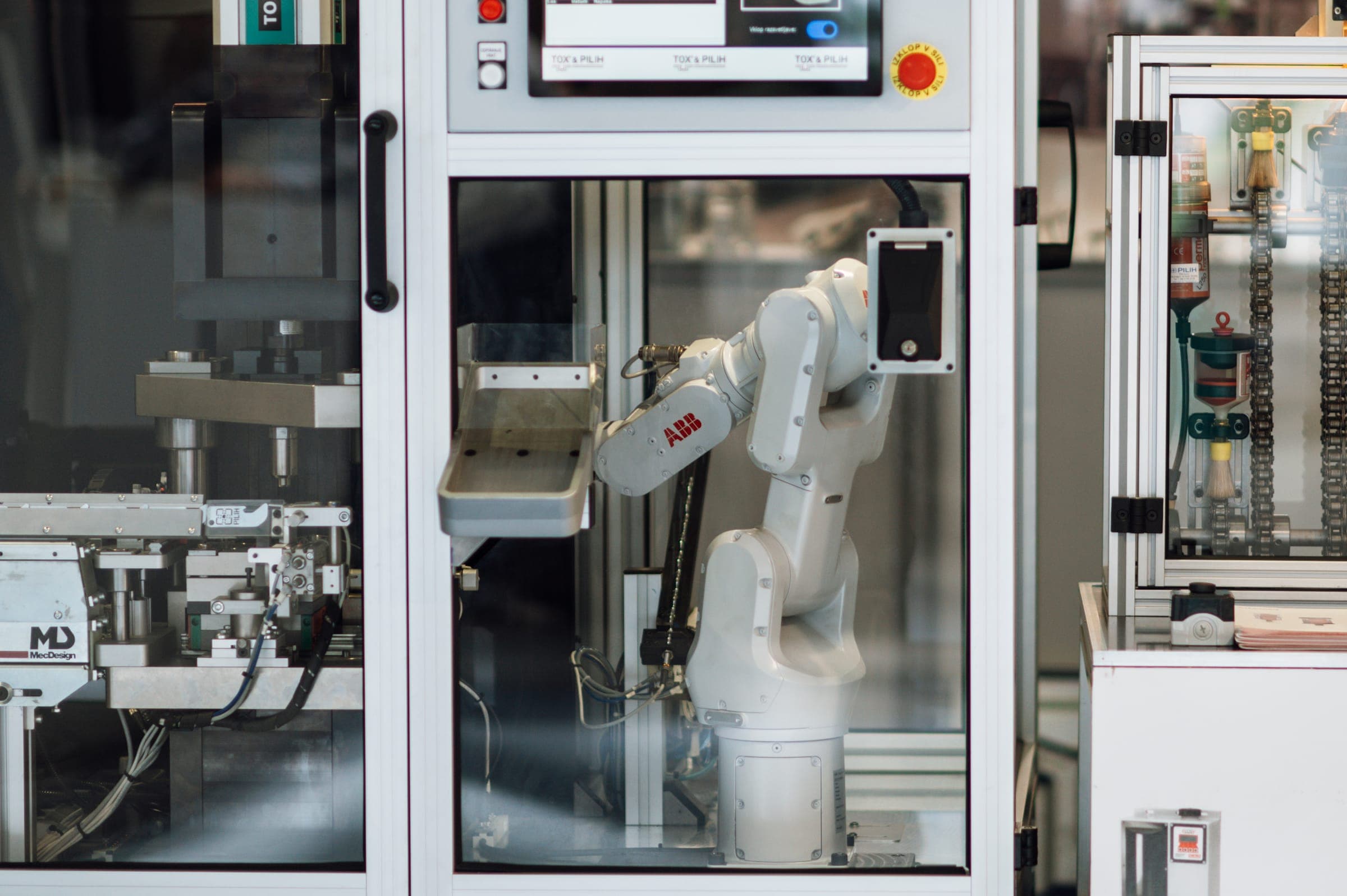 A white industrial robot arm working inside a glass-walled machine cell on a factory floor